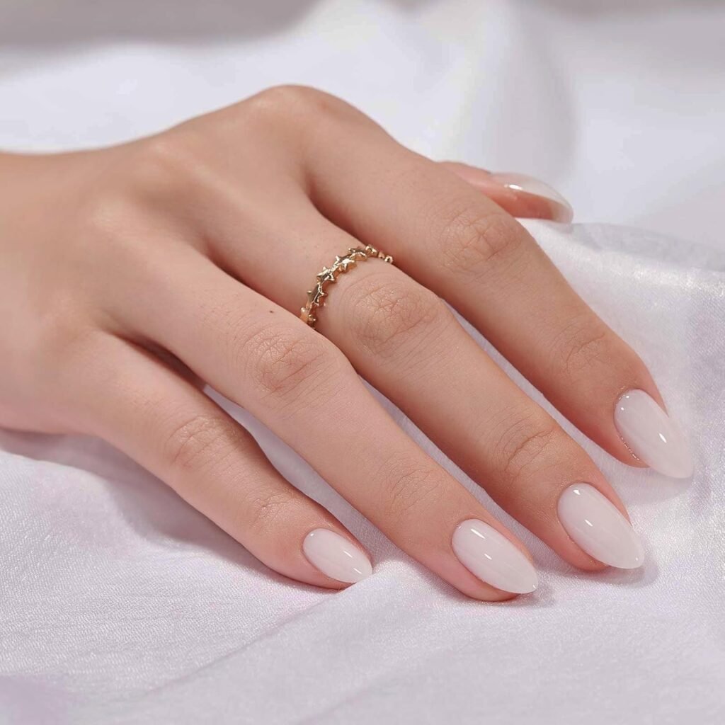 Elegant almond-shaped nude press-on nails with glossy finish, styled with a delicate gold star ring